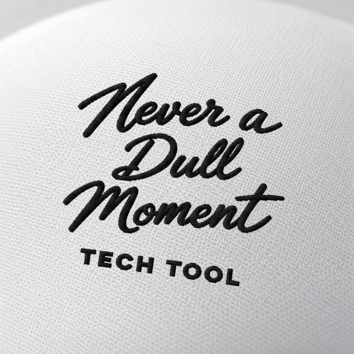 Never a Dull Moment Trucker Hat, oblique macro of Never a Dull Moment script embroidery and Tech Tool signature on white foam | Color: Obsidian (Black / White)